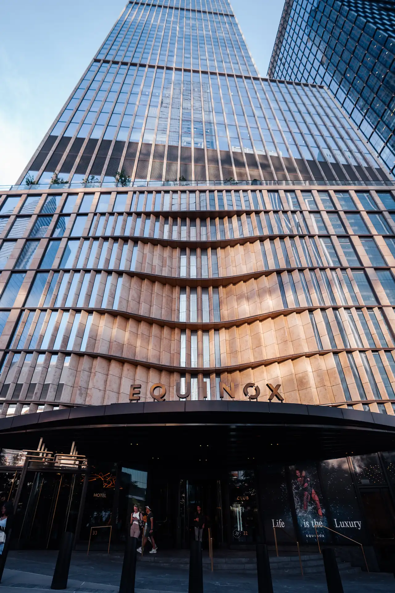 Equinox skyscraper with wave-like glass facade and branded entrance, evoking luxury, movement, and urban prestige
