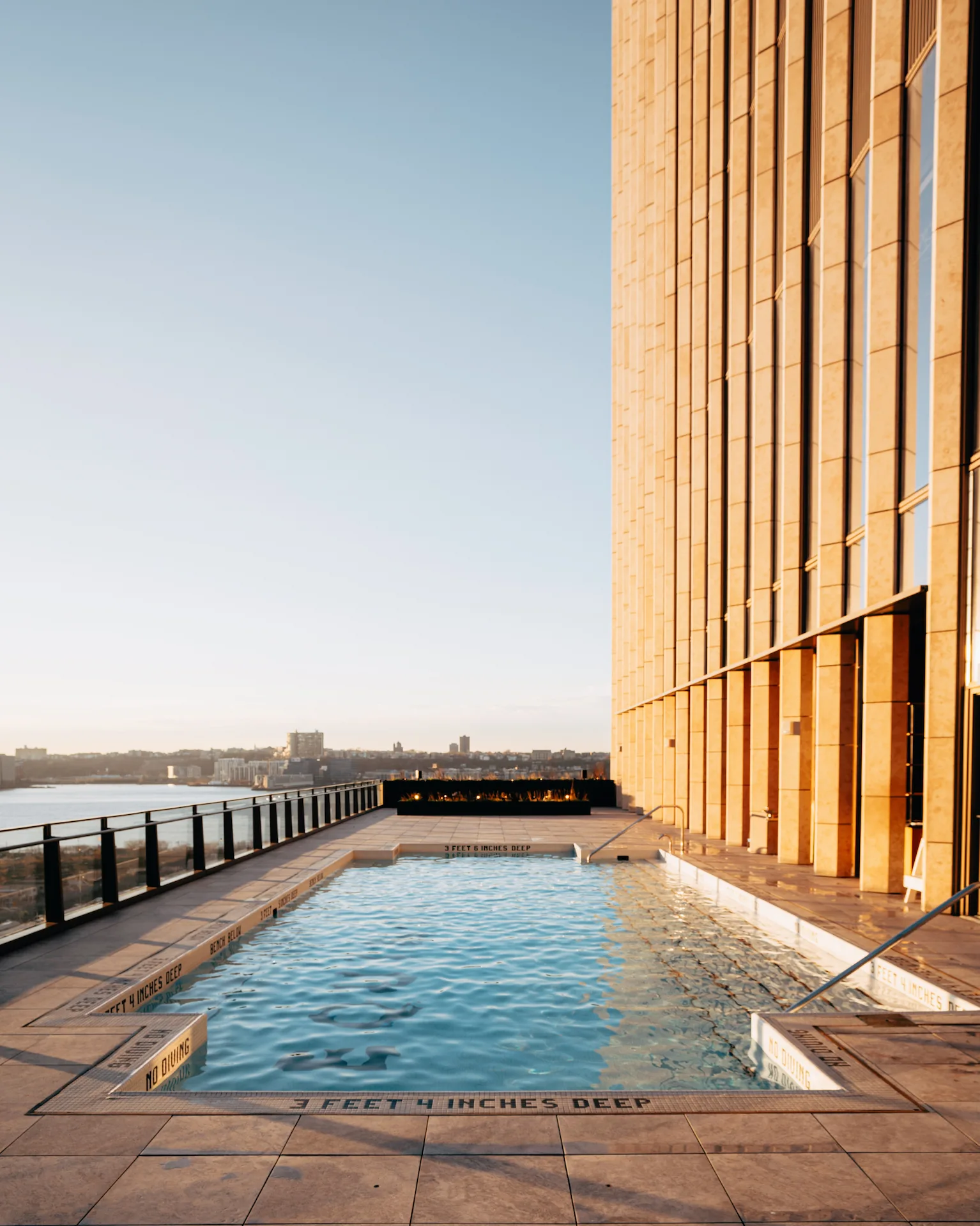 Rooftop pool beside golden high-rise with fire feature and city views, evoking elevated leisure and urban luxury