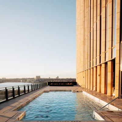 Rooftop pool beside golden high-rise with fire feature and city views, evoking elevated leisure and urban luxury