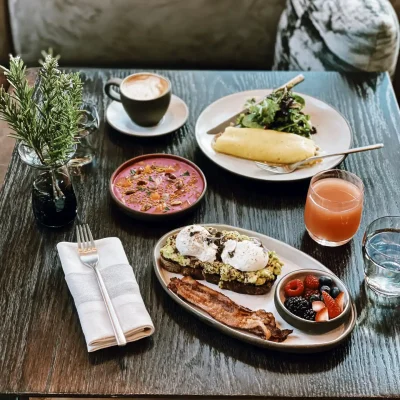 Curated breakfast spread with avocado toast, smoothie bowl, and cappuccino on dark wood table, evoking personalized wellness and morning indulgence