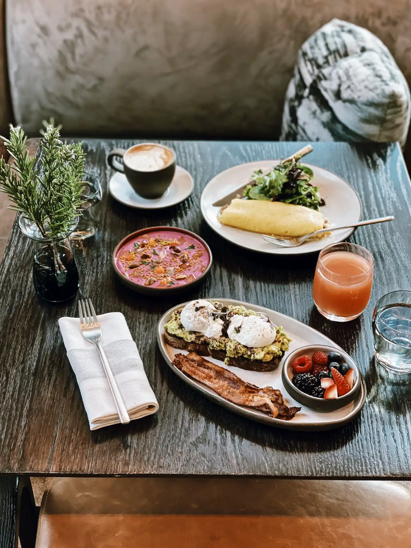 Curated breakfast spread with avocado toast, smoothie bowl, and cappuccino on dark wood table, evoking personalized wellness and morning indulgence