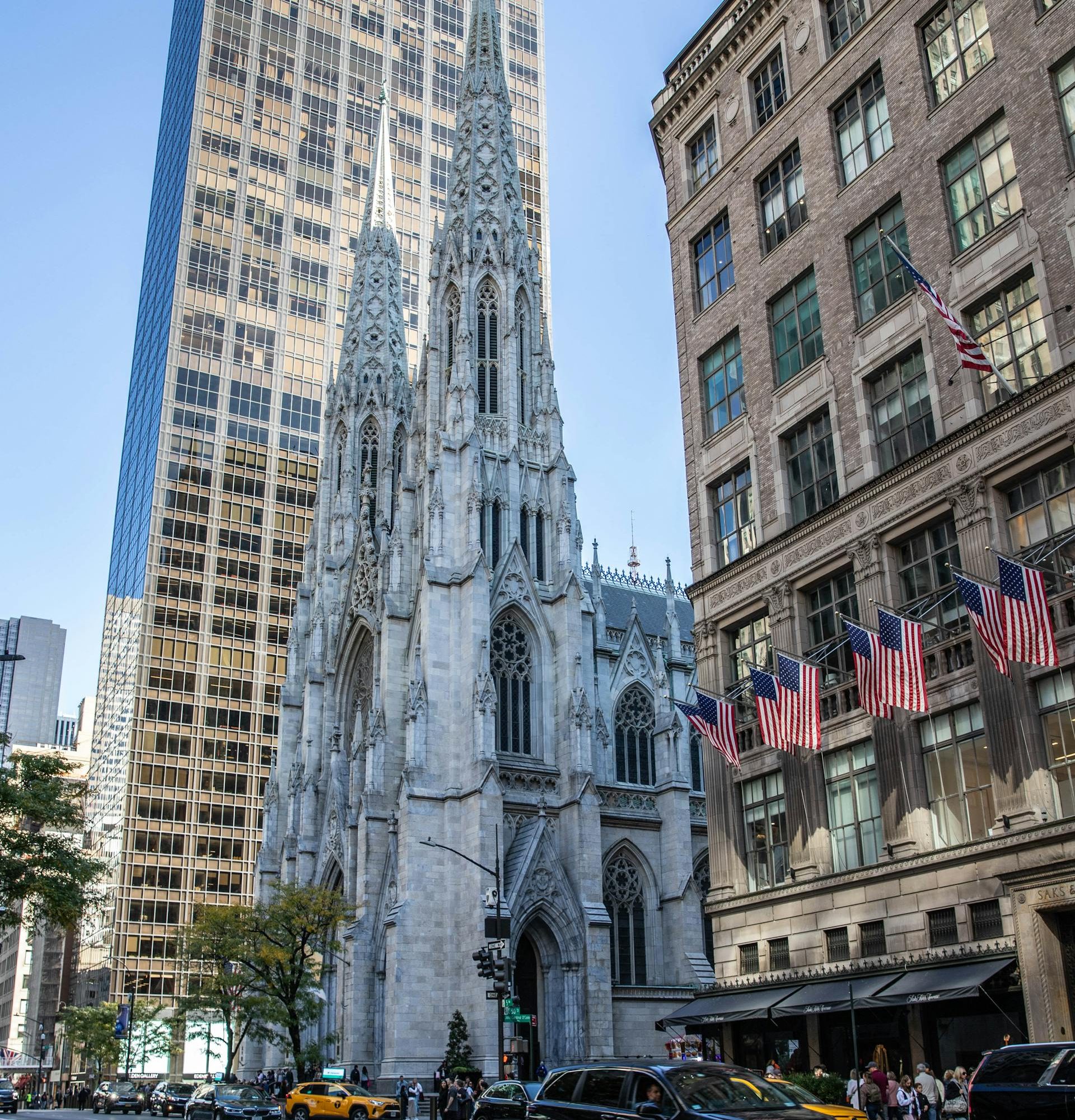 St. Patrick’s Cathedral on Fifth Avenue in Midtown Manhattan, with its Gothic spires rising between modern skyscrapers and busy New York City street traffic in the foreground