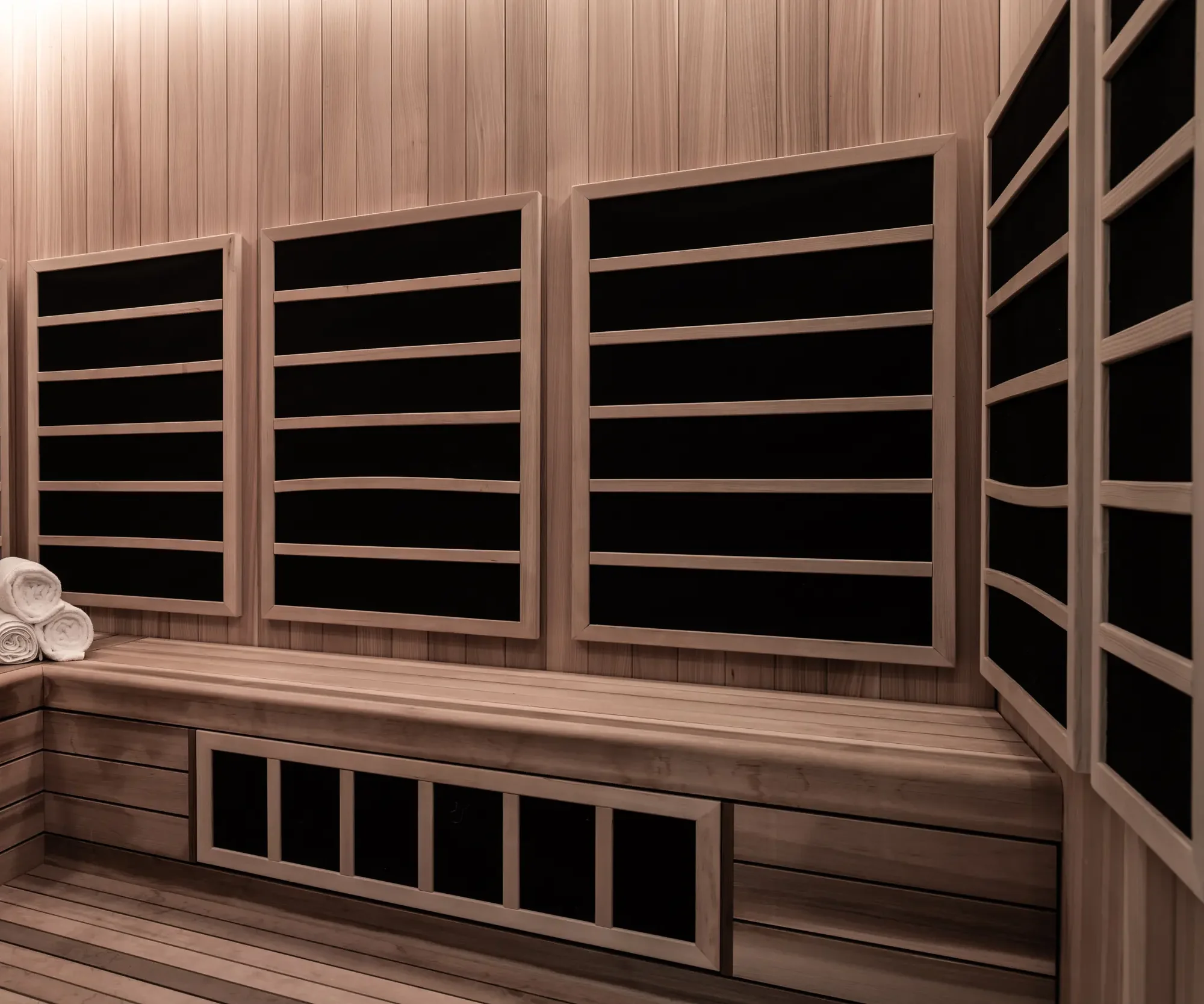 Modern wooden infrared sauna interior with black heating panels, wooden benches, and rolled white towels.
