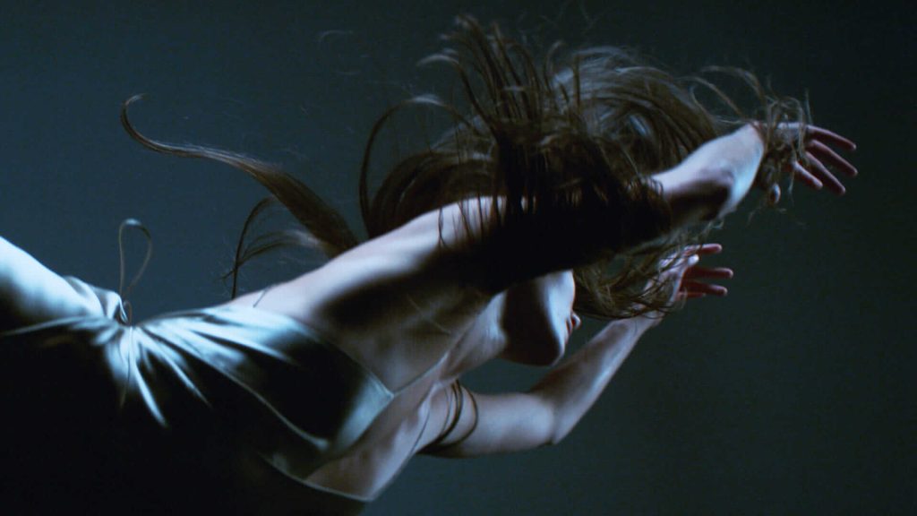 Person in motion with flowing hair and silky outfit, captured in dramatic lighting and expressive pose.