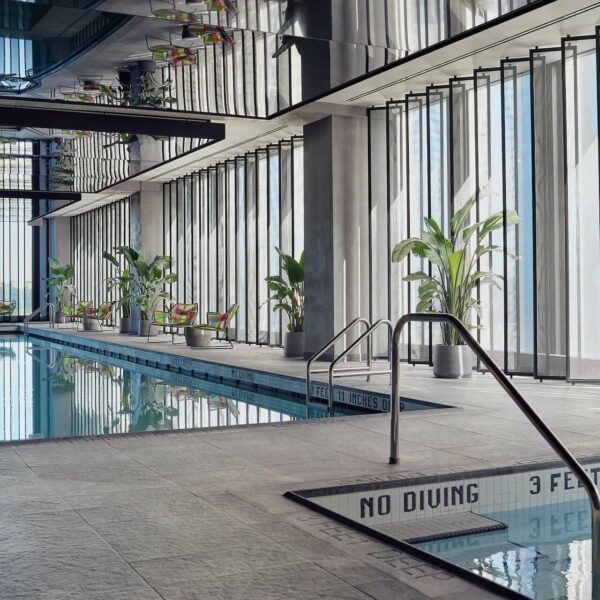 Indoor pool with tall windows, metal frames, plants, NO DIVING sign, and lounge chairs.