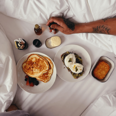 Breakfast in bed with pancakes, avocado toast, and cozy details for a relaxed morning moment.