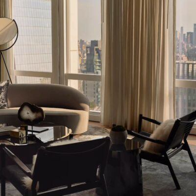 Elegant living room with beige sofa, black coffee table, city skyline view through floor-to-ceiling windows.