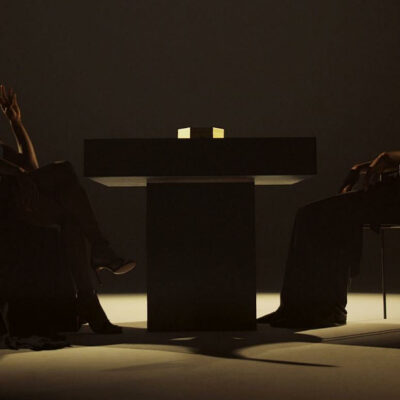 Two people sit across a table in a dark room, lit by a glowing cube that creates a tense, minimalist mood.