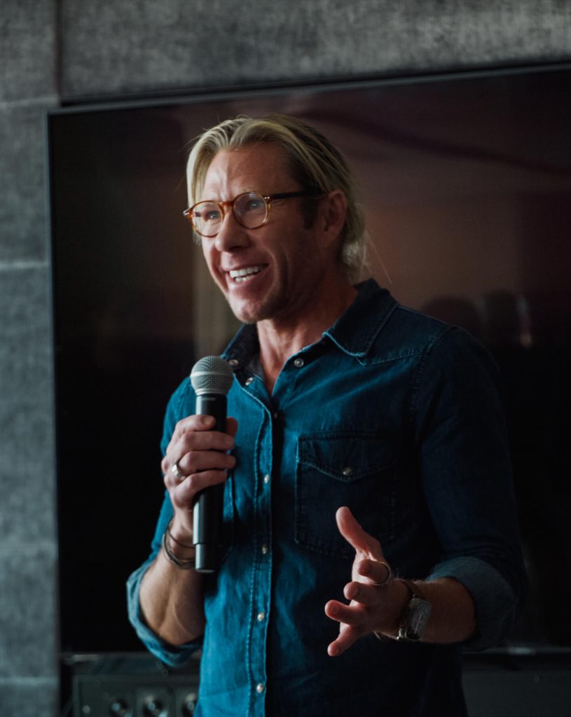 Dr. Matthew Walker speaking into a microphone, wearing glasses and a blue shirt in a presentation setting.