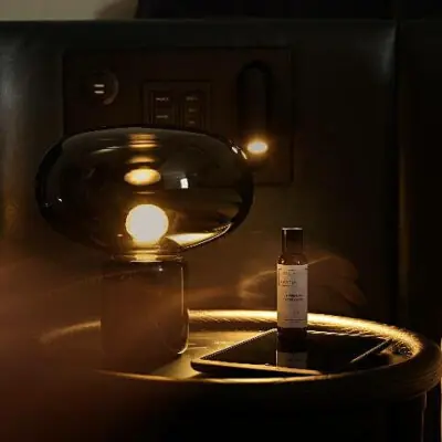 Dimly lit lounge with designer lamp, care products, and soft textures for a cozy, upscale vibe.