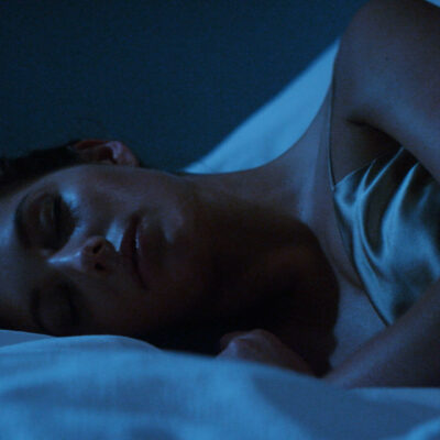 A woman sleeps peacefully at Equinox Hotel, embraced by cutting-edge sleep innovations and calming design.