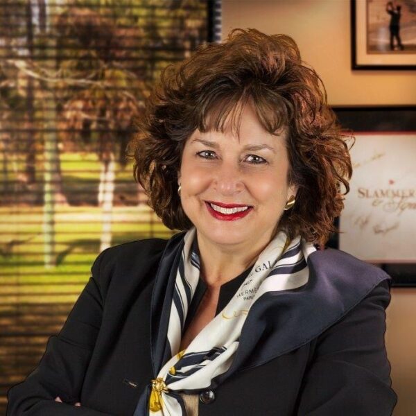 Jane Lucker, smiling with arms crossed in a blazer and scarf, embodying confidence as VP of Sales.