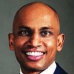 Nathan Loga, smiling in a suit against muted backdrop, radiating warmth and leadership as VP of Guest Experience.