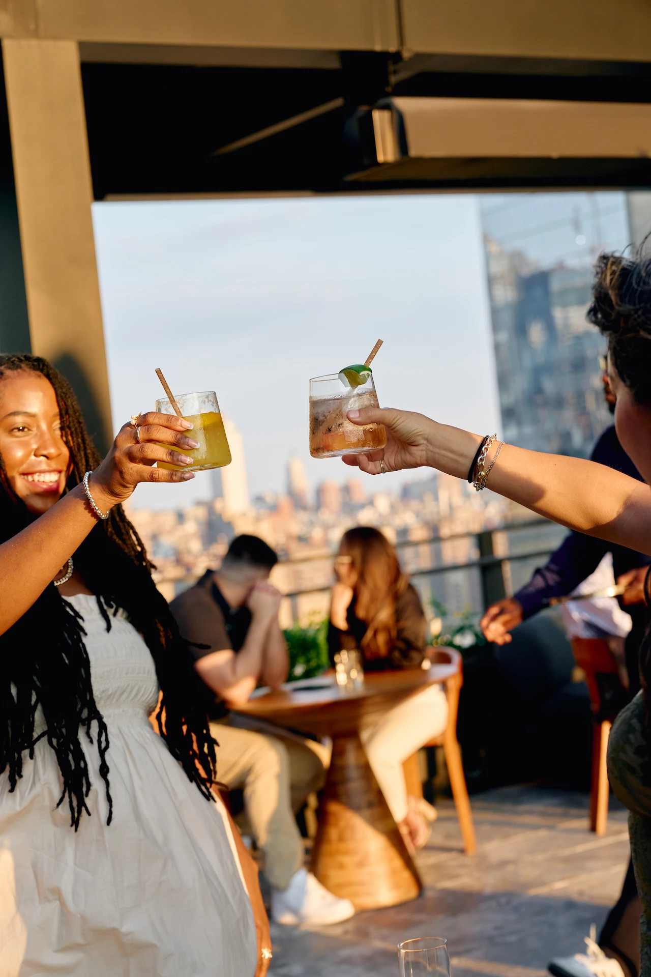 Women toasting with cocktails on Equinox Hotel rooftop terrace, enjoying city views and elegant ambiance.