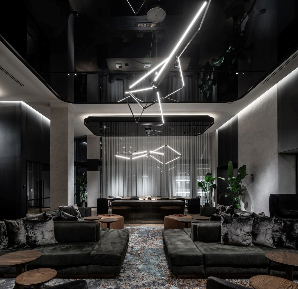 Elegant hotel lobby with large sofas, lush plants, modern lighting, and a central fireplace.