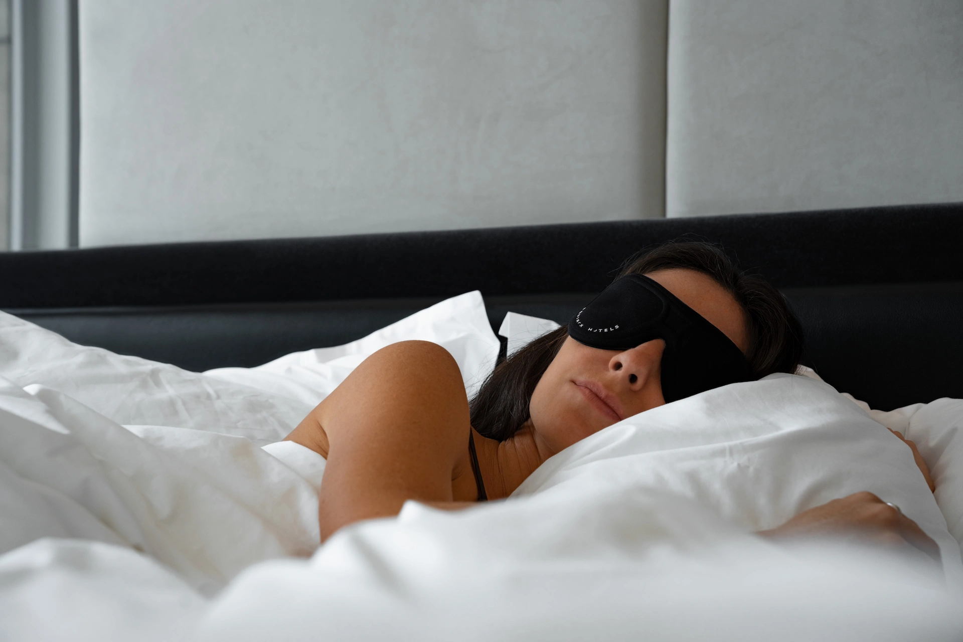 Guest resting in bed with sleep mask, surrounded by soft textures and calming tones in wellness-focused room