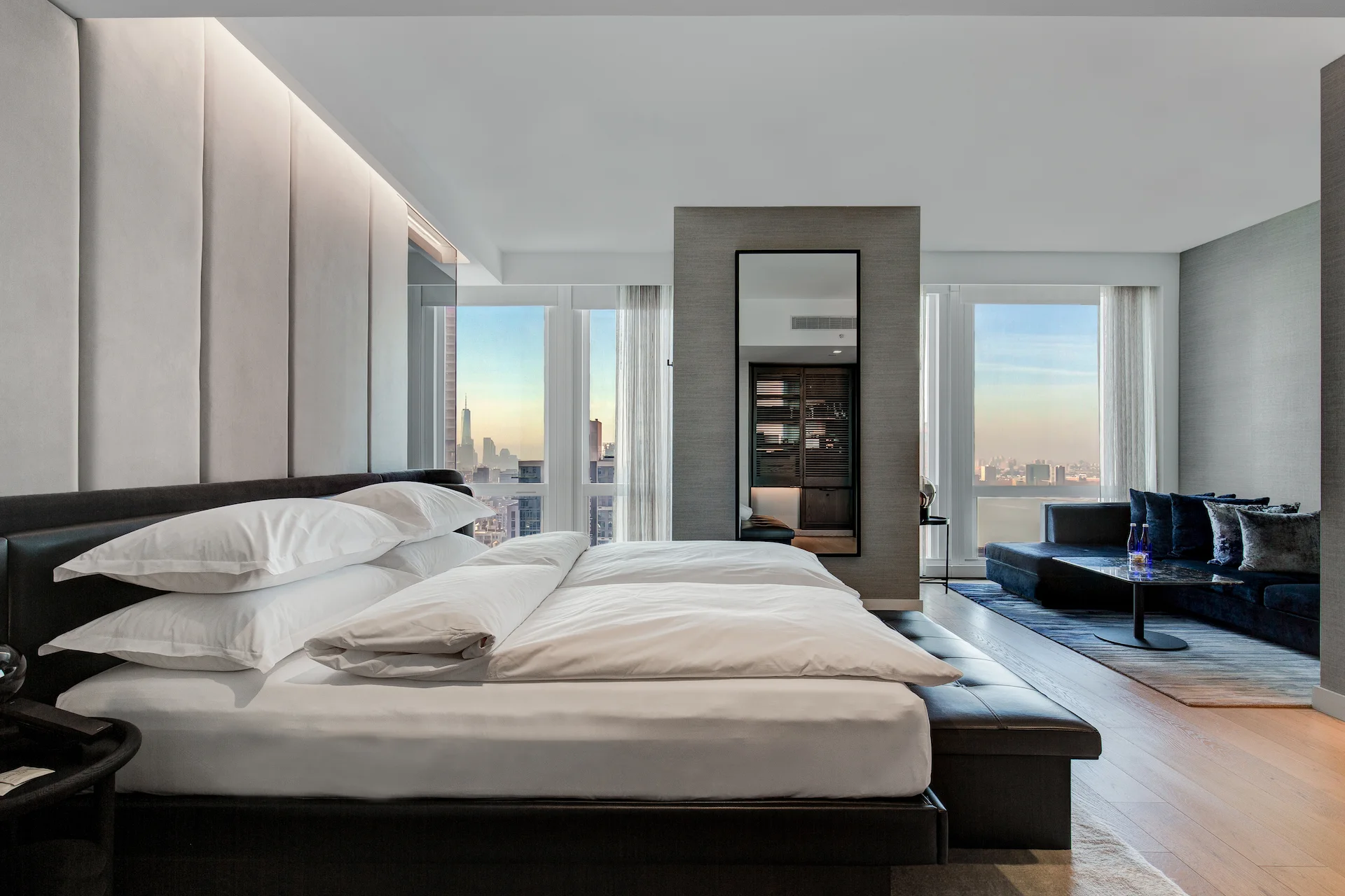 Spacious room with river and city views, large mirror, and cozy living area in the background.