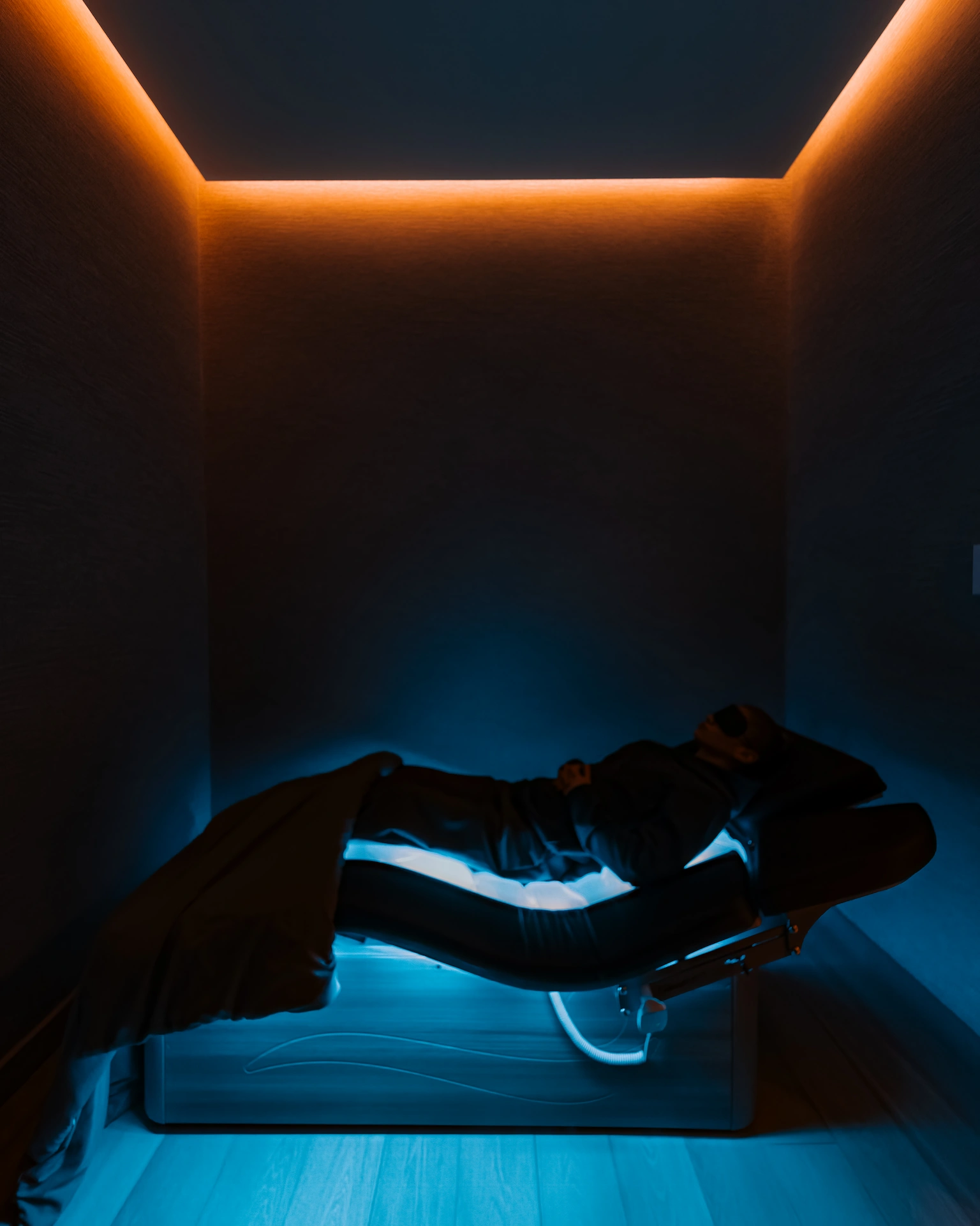 Guest resting in immersive sleep pod with ambient orange and blue lighting during wellness experience