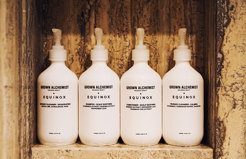 Four Grown Alchemist pump bottles in a stone niche with Equinox branding below.