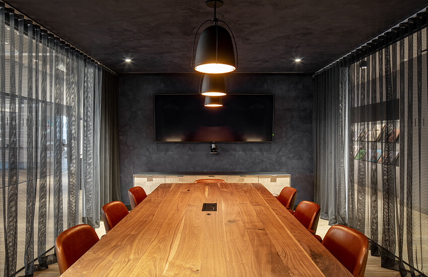 Conference room with long wooden table, brown chairs, black pendants, and a large screen.