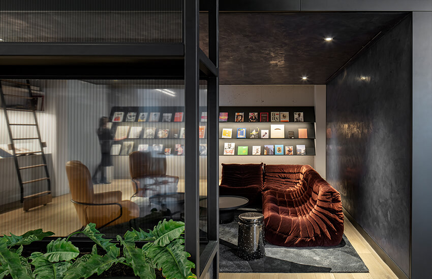 Reading lounge with rust sectional, round tables, glass partition, tan chairs, bookshelves, and plants.