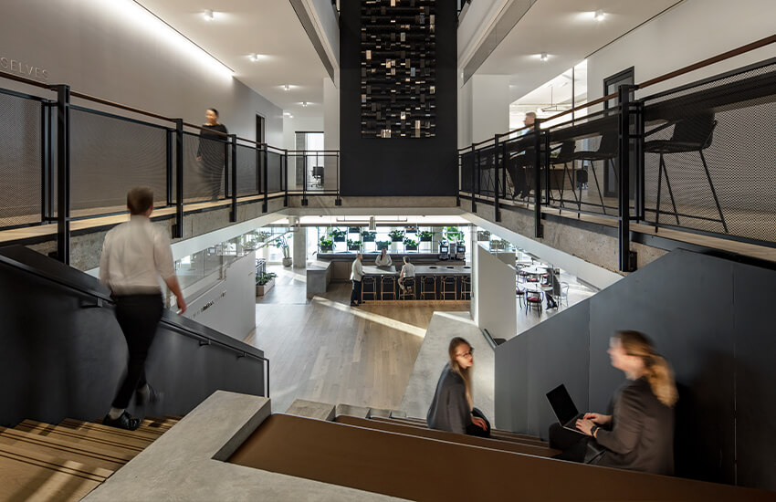 Multi-level office with wide seating stairs, upper walkways, open workspace, and people working.