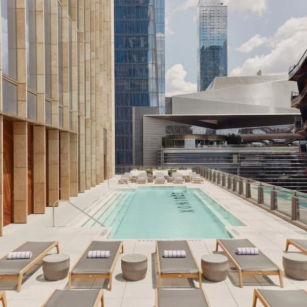 Rooftop pool terrace with lounge chairs, glass railings, and tall modern buildings around.
