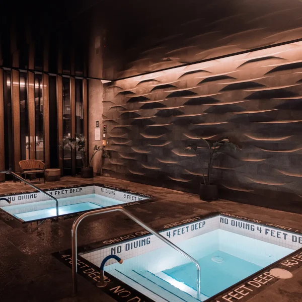 Indoor spa with two square blue soaking pools, depth markings, textured wall, and warm lighting.