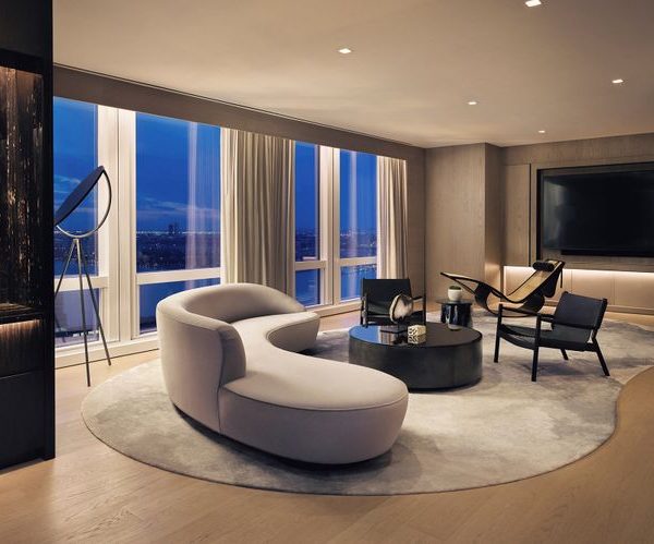 Modern living room with a curved sofa, round rug, low table, and evening city view.