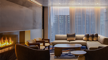 Cozy lounge with large sectional, armchairs, low tables, linear fireplace, and soft city views.