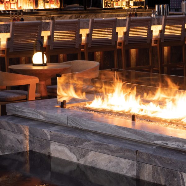 Bar lounge with a glass fire feature, marble ledge, wooden chairs, and warm lantern lighting.