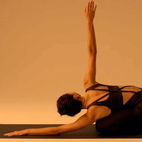 Person in yoga pose on mat, torso twisted, one arm extended upward, warm lighting.