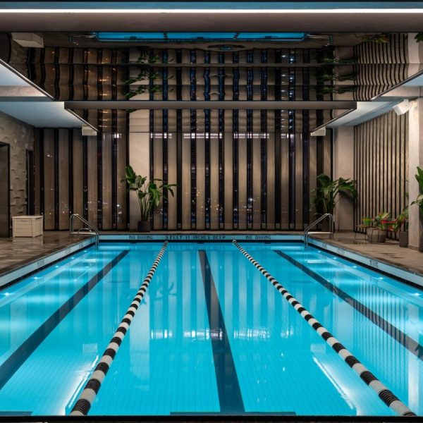 Sleek indoor lap pool with blue water, lane dividers, tall panels, plants, and soft lighting.