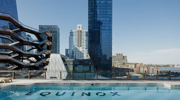 Rooftop pool with “EQUINOX” on the floor overlooking high-rises and the Vessel under a blue sky.