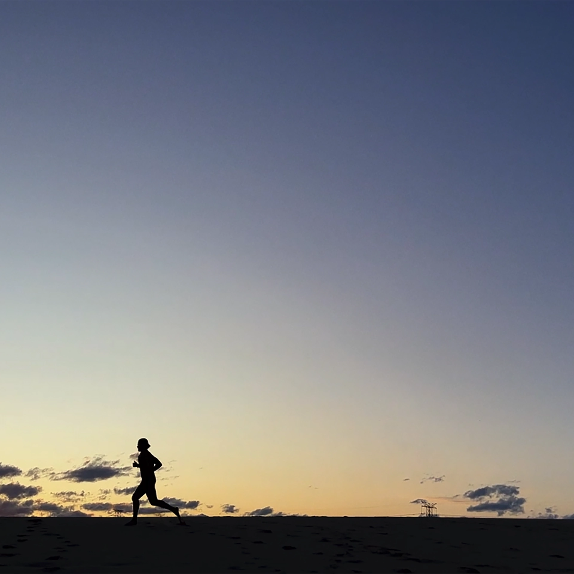 Silhouette of person running at sunrise with orange and blue sky and distant power line structure