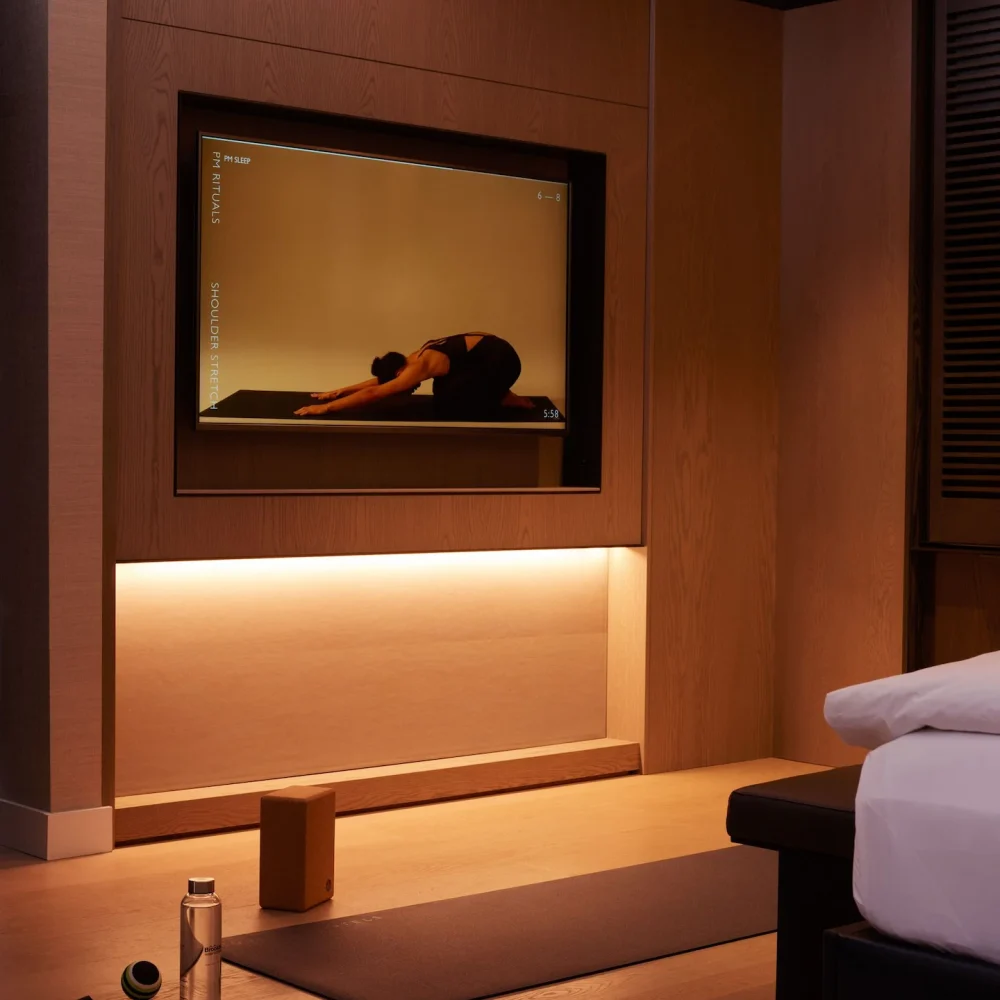 Yoga setup in warmly lit room with screen showing PM Rituals shoulder stretch and wellness props on floor