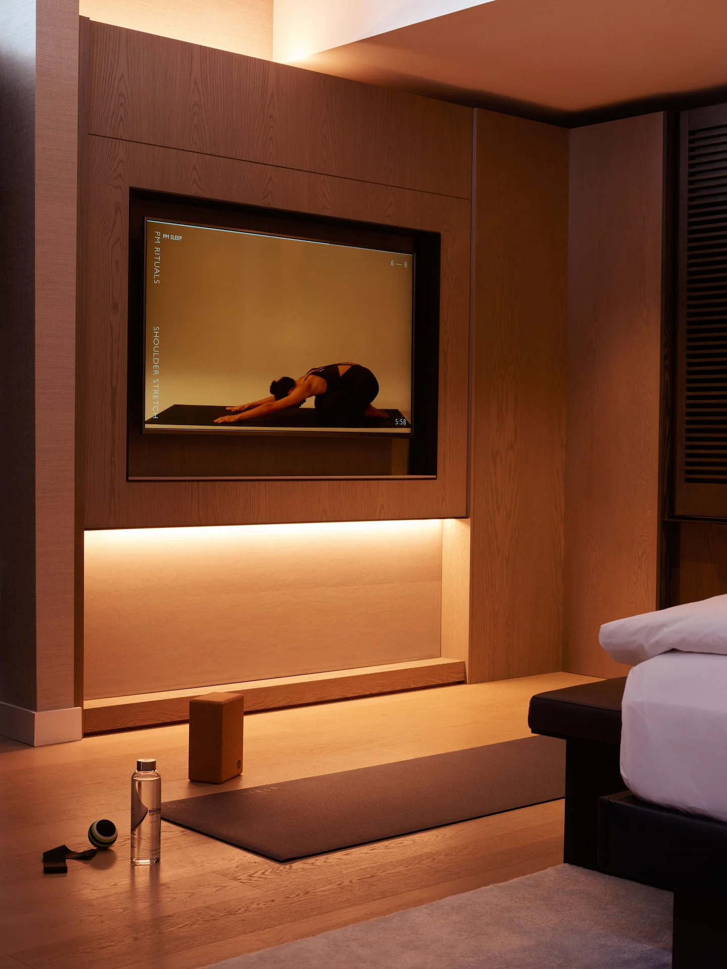 Yoga setup in warmly lit room with screen showing PM Rituals shoulder stretch and wellness props on floor