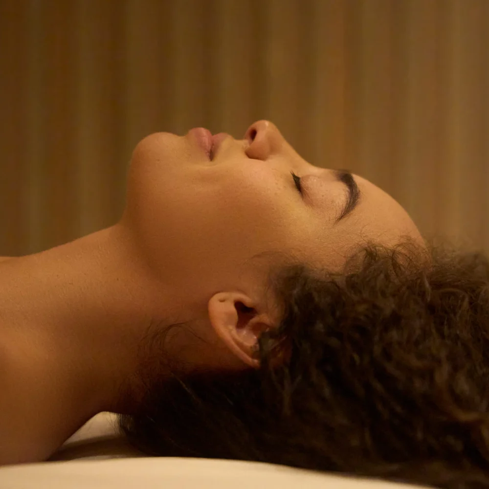 Side profile of person lying down with eyes closed in softly lit room with striped wall background