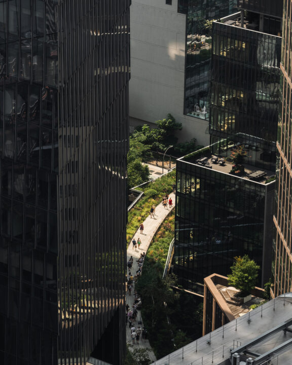 Elevated urban walkway with greenery surrounded by glass buildings and pedestrians in modern cityscape