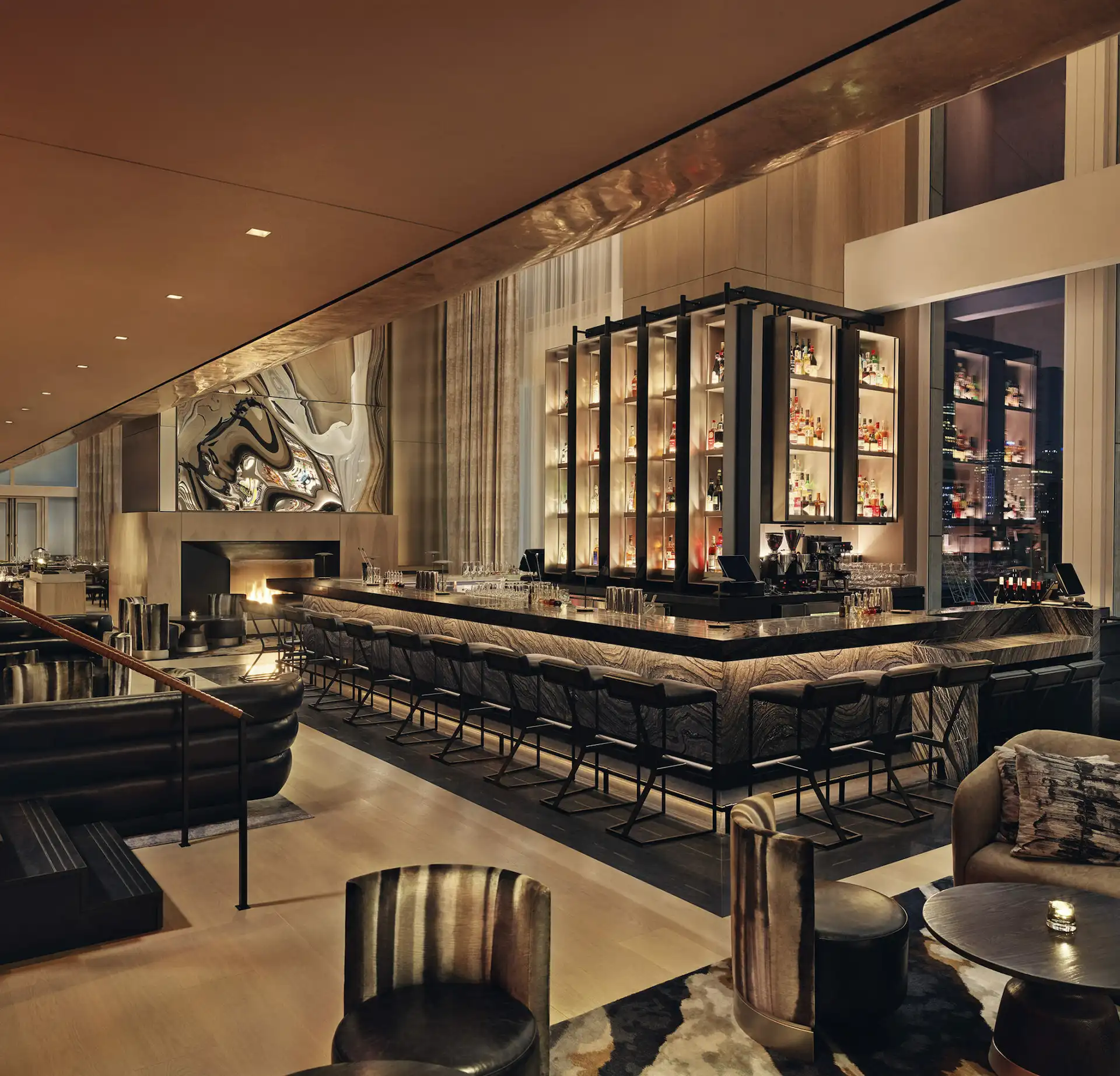 U-shaped bar with high chairs, illuminated liquor shelves, fireplace and city view in elegant lounge