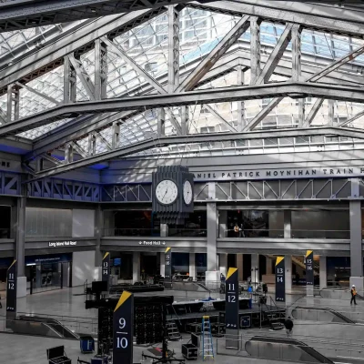 Moynihan Train Hall interior with glass ceiling, steel beams, central clock and digital train boards.