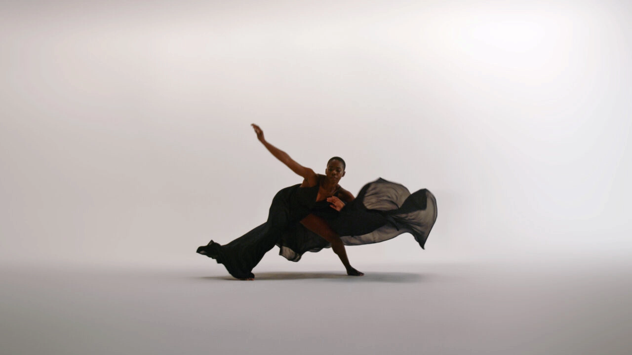 Dancer in flowing black outfit mid-motion against light backdrop, expressing strength and grace