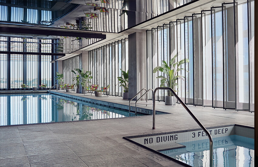 Indoor pool with floor-to-ceiling windows, lounge chairs, potted plants, and reflective ceiling panels