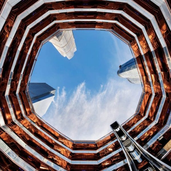 Upward view from inside the Vessel at Hudson Yards showing copper staircases and framed sky with skyscrapers