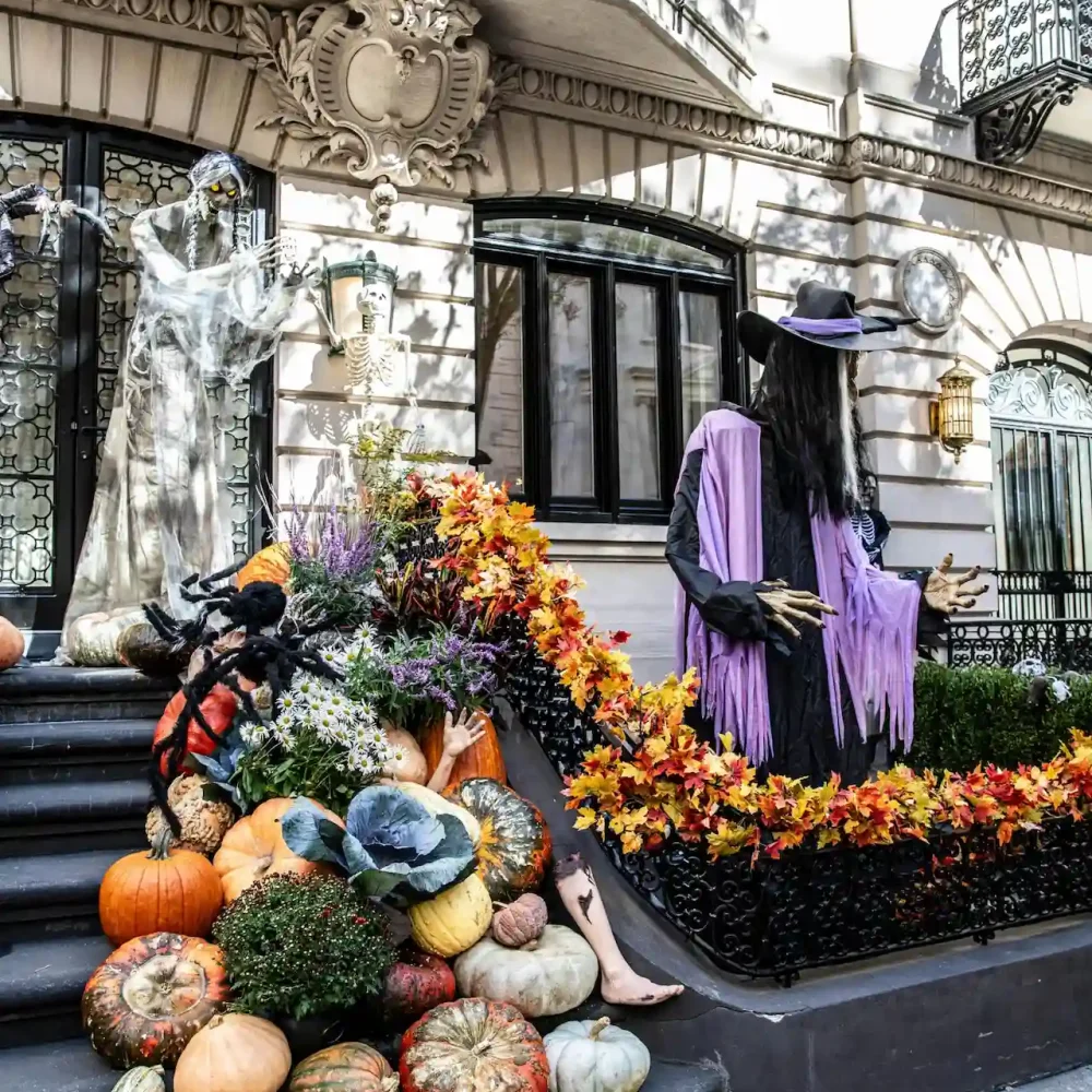 Halloween display with witch, ghost, skeleton, pumpkins, spider, and autumn leaves outside ornate building