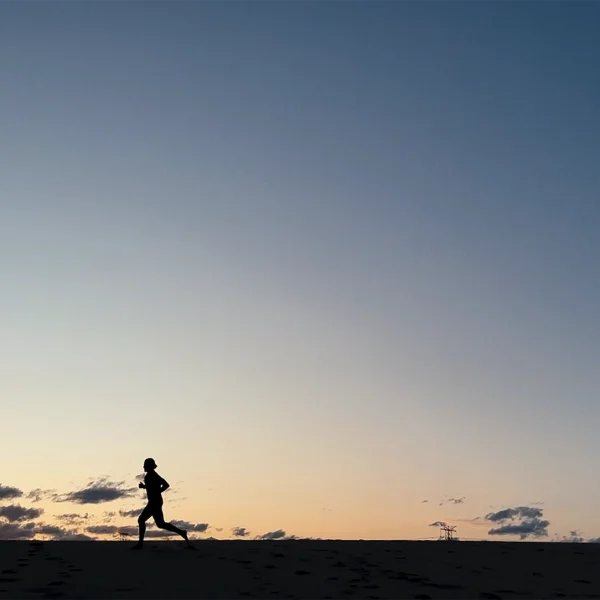 Silhouette of person running at sunrise with orange and blue sky and distant power line structure