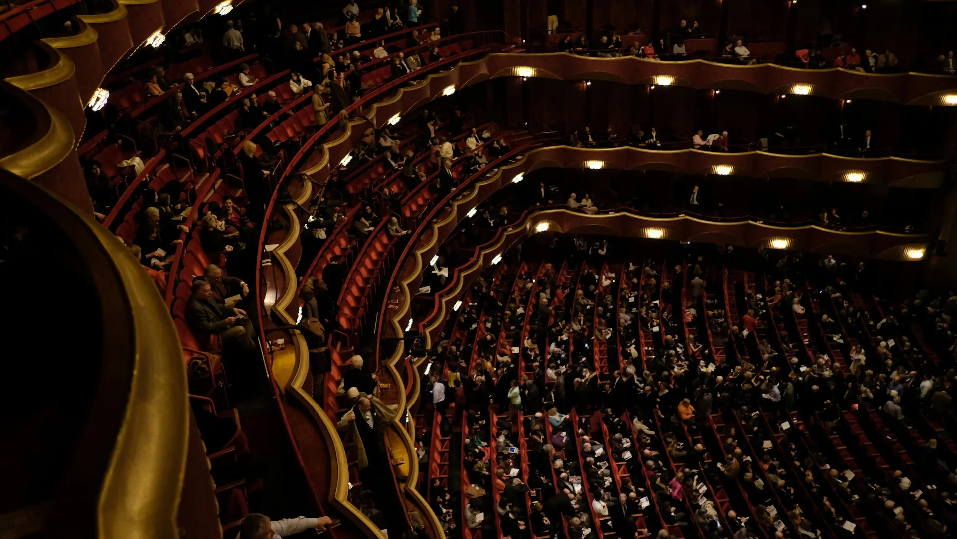 Audience seated in grand theater with ornate balconies and warm lighting during cultural event