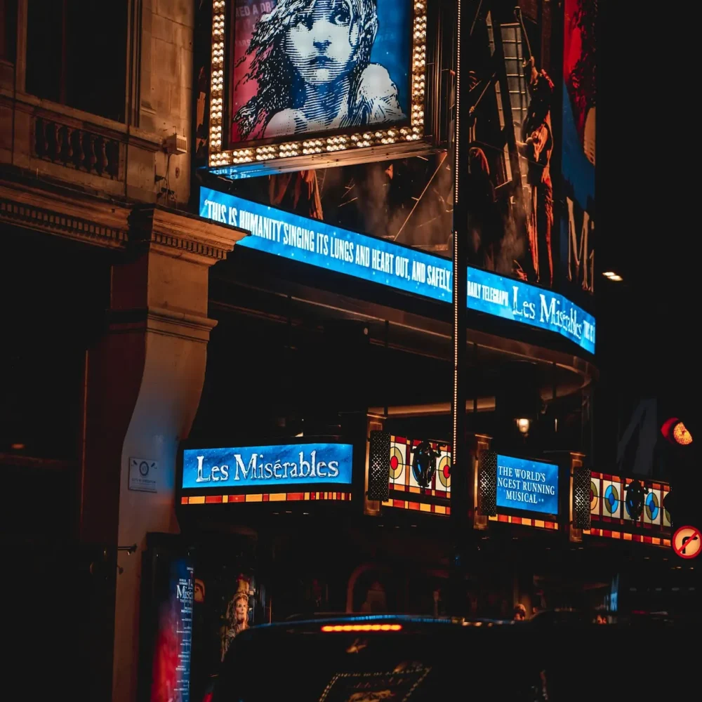 Nighttime theater marquee for Les Misérables, glowing with vibrant blue lights and classic signage on a lively city street.
