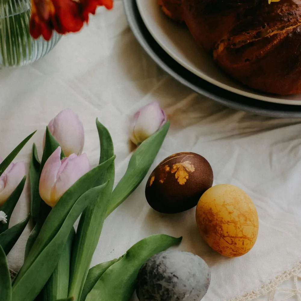 Braided loaf of bread with pastel tulips and decorated Easter eggs on white cloth in spring setting
