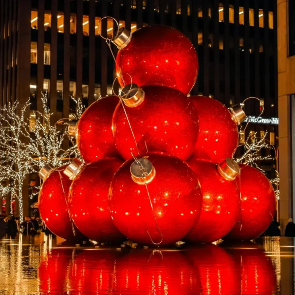 Stacked red Christmas ornaments in city plaza with festive lights, wet reflections and McGraw-Hill building
